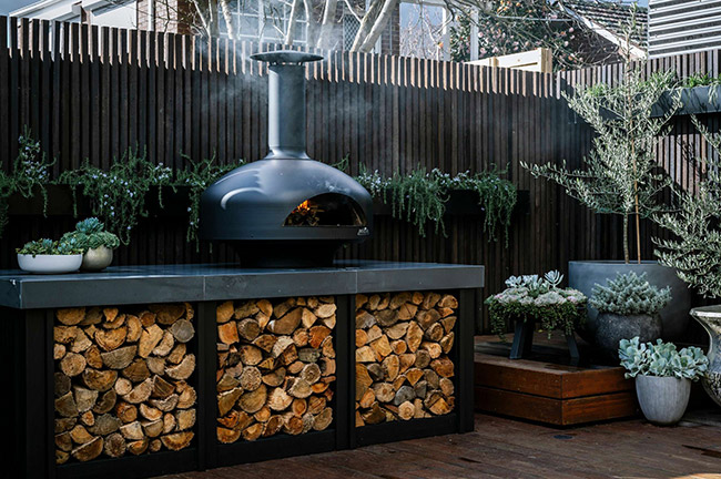 Outdoor fire with stacks of firewood, on plant filled deck